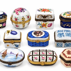 May include: A collection of fourteen small porcelain trinket boxes with hinged metal closures, featuring various shapes including oval, round, square, and hexagonal, decorated with floral patterns, landscapes, and Chinese characters.