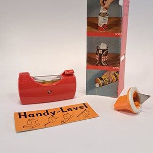 Op de afbeelding: Een rood Handy-Level gereedschap met een heldere waterpas. Het gereedschap wordt getoond met een verpakking die instructies bevat over hoe het gereedschap te gebruiken om blikjes te openen. De verpakking toont drie verschillende soorten blikjes: sap, bier en een blikje met een treklipje.