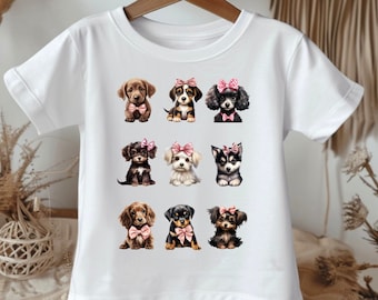 Op de afbeelding: Wit T-shirt met een ontwerp van negen verschillende puppy's die roze strikjes dragen. De puppy's zijn allemaal van verschillende rassen en hebben verschillende uitdrukkingen.