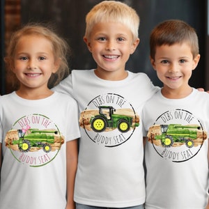 May include: Three white t-shirts with a green tractor and combine harvester graphic. The graphic has the text "Dibs on the Buddy Seat" in a black circle.