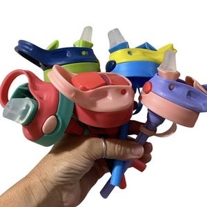 May include: A collection of colorful water bottle lids in various shades of blue, green, yellow, pink, and purple. Each lid features a flip-top design with a silicone spout. The lids are held together, showcasing their diverse color palette.