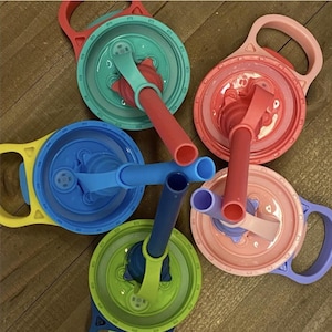 May include: A collection of colorful plastic cup lids with attached handles and straws. The lids are in various colors, including red, blue, green, pink, and yellow. The straws are also in coordinating colors.