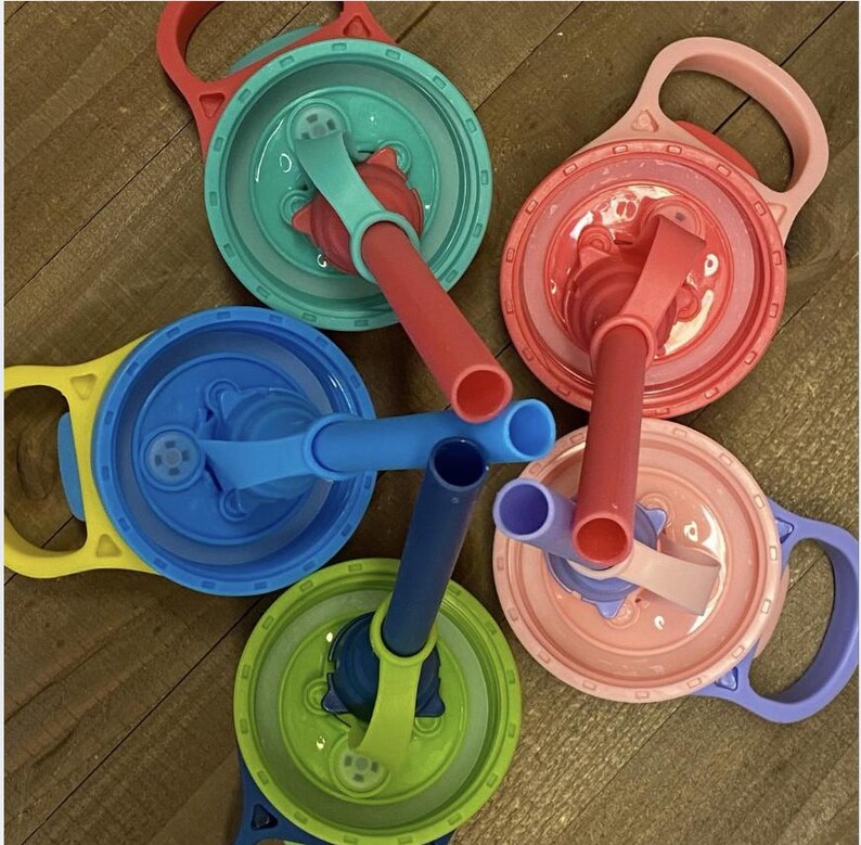 May include: A collection of colorful plastic cup lids with attached handles and straws. The lids are in various colors, including red, blue, green, pink, and yellow. The straws are also in coordinating colors.