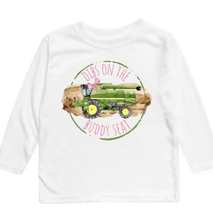 K&ouml;nnte beinhalten: Wei&szlig;es Langarmshirt mit einer Aquarellillustration eines gr&uuml;nen M&auml;hdreschers und einer rosa Schleife. Der Text "Dibs on the Buddy Seat" ist in einem gr&uuml;nen Kreis aufgedruckt.