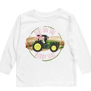 K&ouml;nnte beinhalten: Wei&szlig;es Langarmshirt mit einem gr&uuml;nen Traktor-Motiv und dem Text "Dibs on the Buddy Seat" in einem Kreis. Der Traktor hat gelbe R&auml;der und eine rosa Schleife.