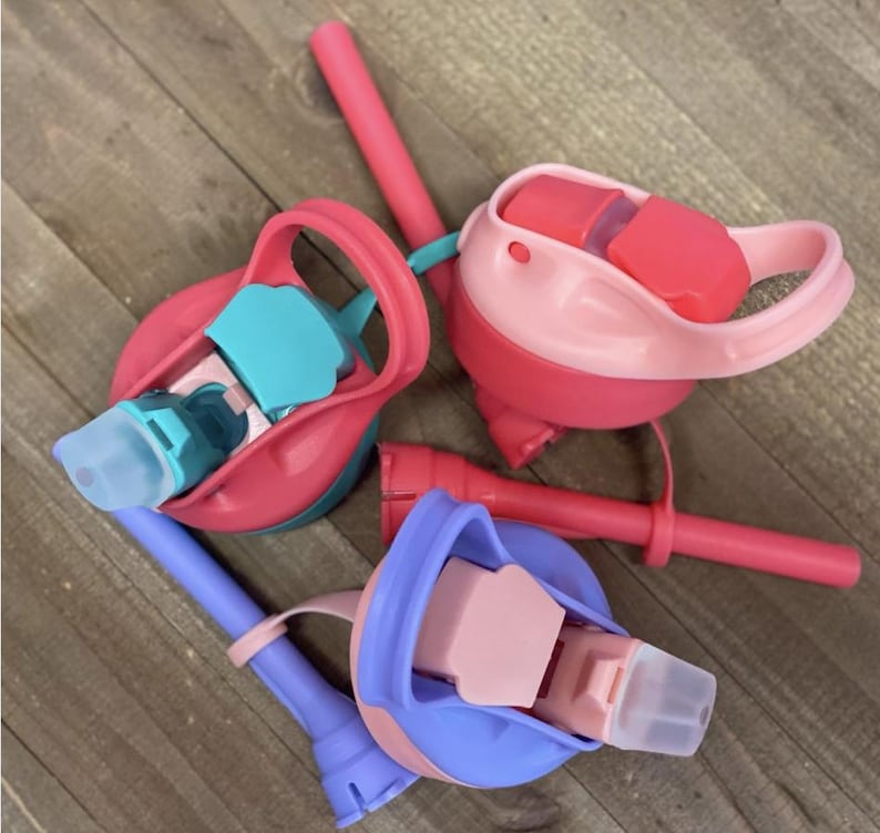May include: Several colorful water bottle lids with attached straws. The lids are in shades of pink, blue, and teal. The straws are a solid pink color. The lids have a flip-top design and are made of plastic.