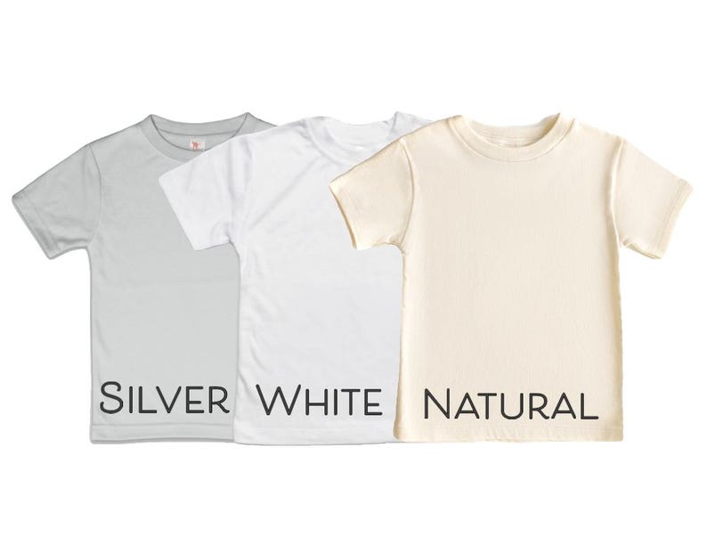 Puede incluir: Tres camisetas de manga corta en diferentes colores: plata, blanco y natural. Las camisetas est&aacute;n dispuestas en plano y la parte inferior de cada camiseta tiene el nombre del color impreso en negro.