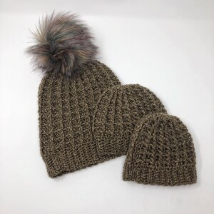 May include: Two brown crocheted hats with a fluffy pom pom on the larger hat. The hats are made with a textured stitch.