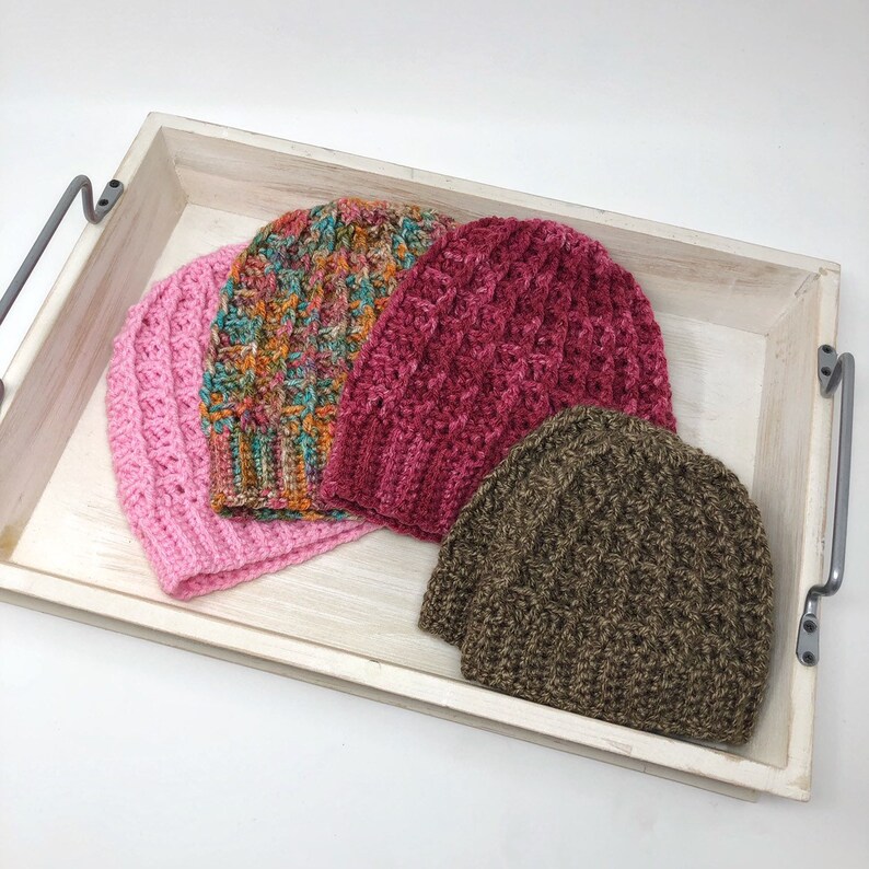 May include: Three crocheted hats in a wooden tray. The hats are pink, brown, and a multi-colored pattern.