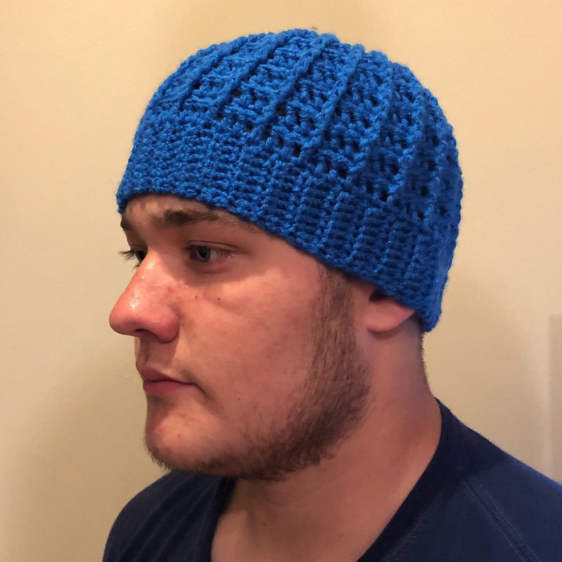 May include: A blue crocheted beanie hat with a textured pattern. The hat is worn by a person with a beard.
