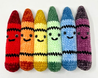 May include: Six crocheted crayon toys with smiling faces. The crayons are red, orange, yellow, green, blue, and purple.