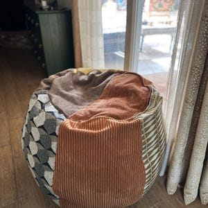 May include: A large, brown, beige, and gray beanbag chair with a corduroy texture. The chair is sitting on a wooden floor.