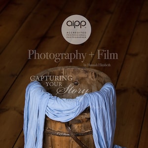 May include: A wooden bucket with a blue fabric draped over the top. The bucket is on a wooden floor. The text "Capturing Your Story" is written on the fabric. The text "Photography + Film by Hannah Elizabeth" is written above the bucket.