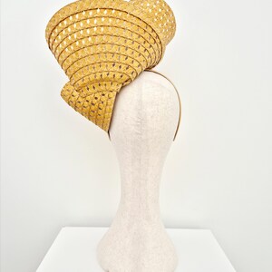 Peut inclure: Un chapeau fascinateur en paille jaune moutarde dot&eacute; d'un large bord sculpt&eacute; et tress&eacute; avec un motif ajour&eacute; en losanges. Le chapeau est mont&eacute; sur un serre-t&ecirc;te fin de couleur neutre, pr&eacute;sentant une forme et une texture structur&eacute;es et asym&eacute;triques.