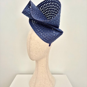 Peut inclure: Un chapeau fascinateur bleu marine profond fabriqu&eacute; en paille tress&eacute;e avec un motif en losanges ajour&eacute; distinct. La coiffe pr&eacute;sente un design haut, sculptural et asym&eacute;trique qui se courbe vers le haut et vers l'ext&eacute;rieur depuis la base.