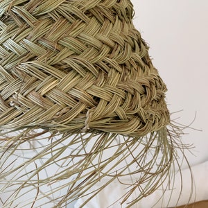 May include: A woven lampshade made of natural materials, with a fringe of long, thin strands hanging from the bottom edge.