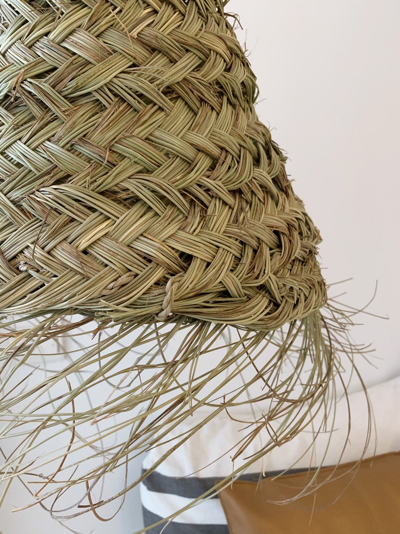 May include: A woven lampshade made of natural materials, with a fringe of long, thin strands hanging from the bottom edge.