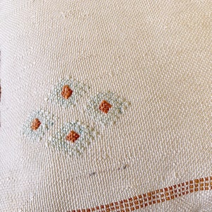 May include: A close-up of a white fabric with a brown border and a small embroidered design of three flowers in blue and orange.