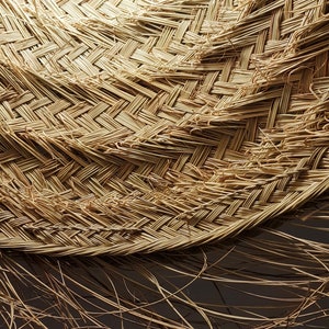 May include: Close-up of a woven straw hat with a natural brown color. The hat is made of tightly woven strands of straw, creating a textured surface. The hat is slightly curved, giving it a rounded shape.