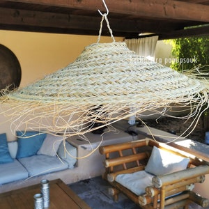 May include: A large, woven, straw lampshade hangs from the ceiling of a patio. The lampshade is light brown and has a wide brim. The patio is furnished with a couch and a chair.