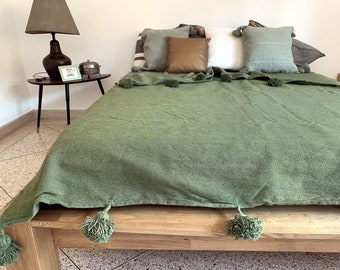 May include: A green throw blanket with pom-poms on a wooden bed frame. The blanket is made of a soft, textured fabric.