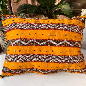 May include: A yellow and brown patterned throw pillow with sequins. The pillow is made of a soft, woven fabric and has a fringe detail.