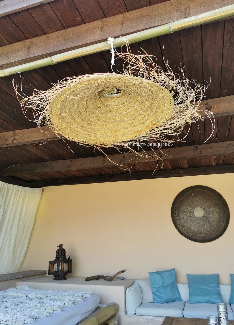 May include: A large, round, woven, straw lampshade hangs from a wooden ceiling. The lampshade is made of natural materials and has a rustic, bohemian style.