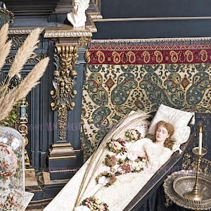 May include: A person with light brown hair wearing a white lace dress lies inside a black coffin. The coffin is lined with white fabric and decorated with dried flower bouquets. A human skull sits on the floor near the base of the coffin.