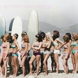 Foto fija en color mod de los años 60 de un grupo de chicas surfistas en bikini posando junto a un estante de tablas de surf Tarjeta de felicitación de 5x7