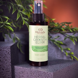 May include: A brown glass bottle with a clear spray nozzle, labeled "Menada Herbal Growth Elixir". The bottle contains 120 ml of liquid and is sitting on a textured surface.