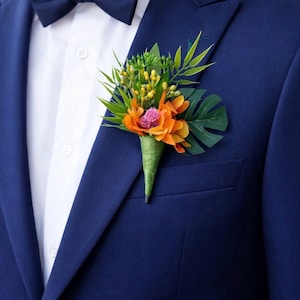 May include: A navy blue suit jacket with a white button-down shirt and a matching navy blue bow tie. A floral boutonniere is pinned to the lapel, featuring orange petals, a small pink flower, green tropical leaves, and yellow berries.