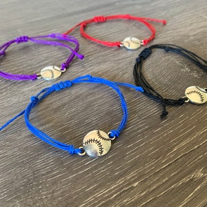 May include: Four adjustable friendship bracelets with a silver baseball charm. The bracelets are red, purple, blue, and black.