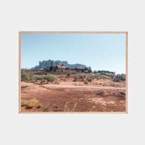 May include: A photograph of a small town in the desert, with a mountain range in the background. The town is made up of a few buildings, including a church, and is surrounded by trees and bushes. The ground is covered in dirt and rocks.