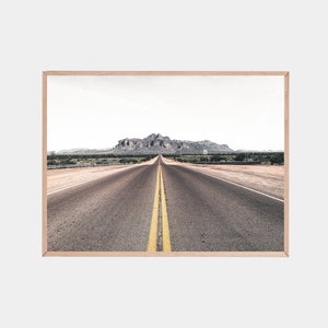 May include: A long, straight, paved road with yellow lines down the center, leading towards a mountain range in the distance. The road is surrounded by desert landscape.
