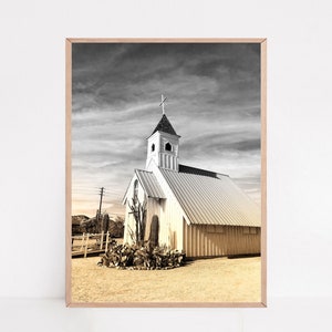 May include: A black and white photograph of a white church with a steeple and a cross on top. The church is in a desert setting with a few trees and a fence in the foreground.