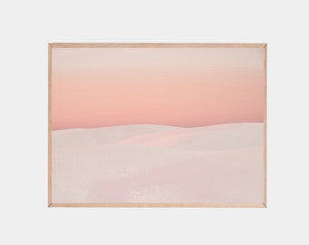 May include: A framed print of a desert landscape with soft pink and white hues. The image features rolling sand dunes under a pale pink sky.