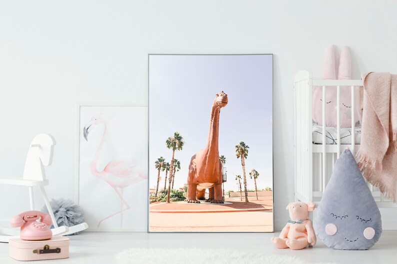 May include: A framed print of a large, brown dinosaur standing in a desert landscape with palm trees. The dinosaur is facing forward with its head tilted up. The sky is blue and the sand is a light brown.