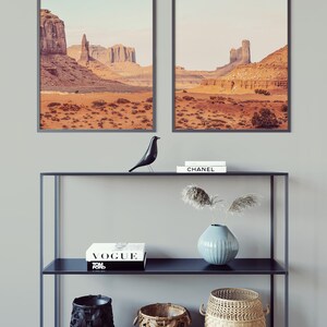 Peut inclure: Deux photographies de paysage encadr&eacute;es d'une sc&egrave;ne d&eacute;sertique avec des formations rocheuses rouges. Une &eacute;tag&egrave;re noire &agrave; deux niveaux contient une figurine d'oiseau noir, un livre blanc avec le mot "VOGUE" sur la couverture, un vase bleu avec des fleurs s&eacute;ch&eacute;es et trois paniers tiss&eacute;s.