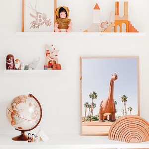 May include: A white shelf with a globe, wooden toys, a doll, and a framed print of a dinosaur. The shelf is above three wicker baskets.