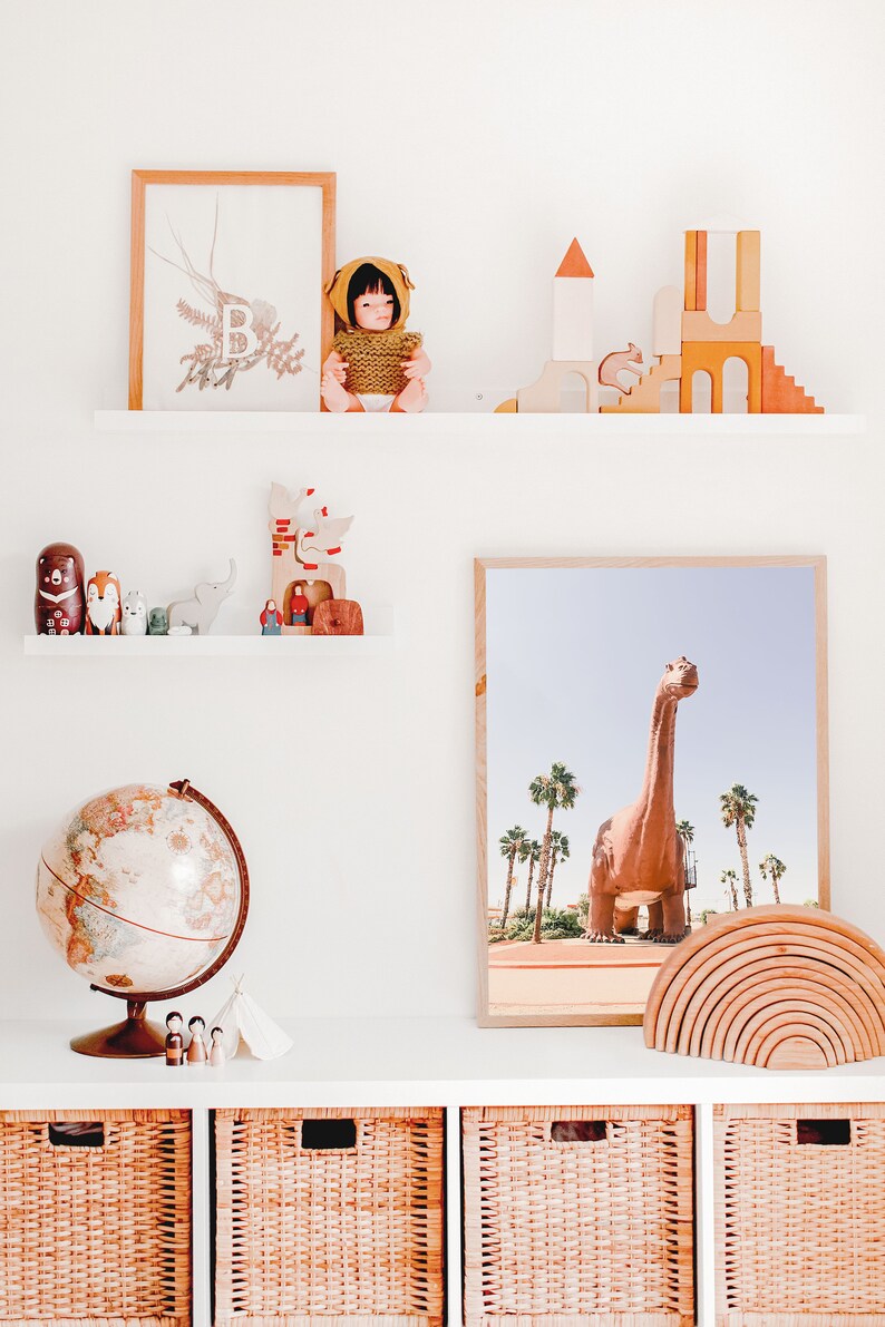 May include: A white shelf with a globe, wooden toys, a doll, and a framed print of a dinosaur. The shelf is above three wicker baskets.