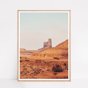 Peut inclure: Une photographie d'un paysage d&eacute;sertique avec une grande formation rocheuse en arri&egrave;re-plan. La formation rocheuse est de couleur brun clair et a une forme irr&eacute;guli&egrave;re et dentel&eacute;e. Le premier plan est recouvert de sable et de petits arbustes. Le ciel est bleu clair et il y a des nuages au loin.
