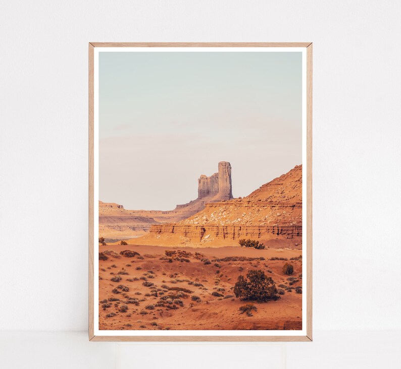 Peut inclure: Une photographie d'un paysage d&eacute;sertique avec une grande formation rocheuse en arri&egrave;re-plan. La formation rocheuse est de couleur brun clair et a une forme irr&eacute;guli&egrave;re et dentel&eacute;e. Le premier plan est recouvert de sable et de petits arbustes. Le ciel est bleu clair et il y a des nuages au loin.
