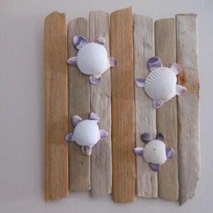May include: A decorative wall hanging featuring four white seashells with purple accents, arranged on a backdrop of vertical wooden planks in varying shades of brown and gray. The seashells are arranged to resemble turtles.