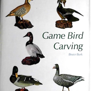 Puede incluir: Un libro titulado "Game Bird Carving" de Bruce Burk, que presenta cinco p&aacute;jaros tallados: una codorniz marr&oacute;n y blanca, un pato de madera verde y blanco, un pato marr&oacute;n y blanco, un ganso gris y blanco y un pato silvestre.