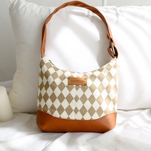 May include: A tan and white checkered canvas tote bag with a brown leather strap and bottom. The bag has a metal tag that says "handmade".
