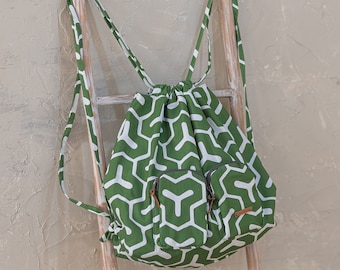 May include: A green drawstring backpack with a white geometric pattern. The backpack has two zippered pockets on the front and a brown leather pull tab.