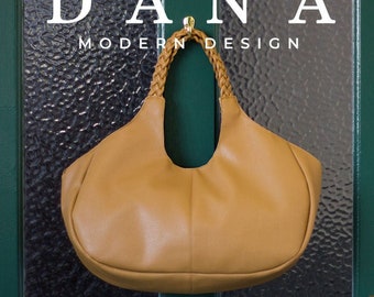 May include: A tan leather handbag with a braided handle hanging on a green door. The bag has a rounded shape and a wide opening. The text "DANA MODERN DESIGN" is above the bag.