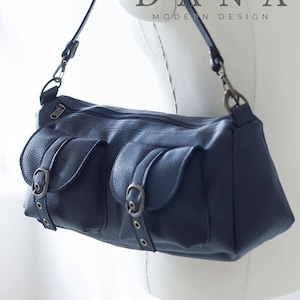 May include: A dark blue leather shoulder bag with multiple pockets and a buckle closure. The bag has a long adjustable strap and the brand name "DANA MODERN DESIGN" is printed on the front.