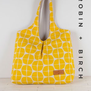 May include: A yellow tote bag with a geometric pattern. The bag has a brown leather tag that says "Handmade".