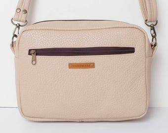 Può includere: Una borsa a tracolla beige chiaro con una cerniera marrone e un'etichetta in pelle marrone che dice "HANDMADE".